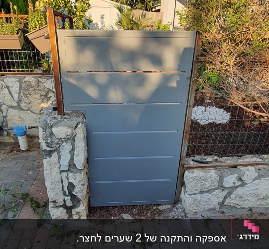 שער מתכת אפור עם מסגרת עץ ואבנים מסביב